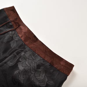 Op de afbeelding: Zwarte broek met een bruin bloemenpatroon en een bruine satijnen tailleband.