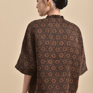 May include: A brown and black patterned short-sleeved shirt with a ruffled collar.