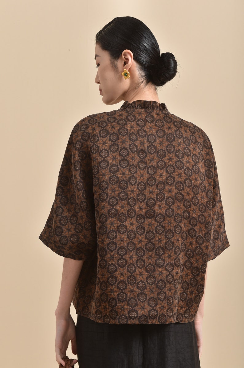 May include: A brown and black patterned short-sleeved shirt with a ruffled collar.