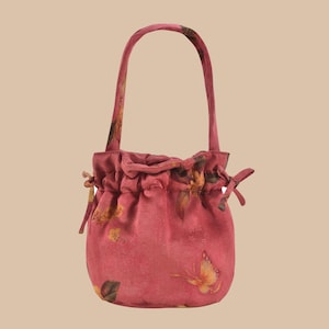 Può includere: Una piccola borsa rosa con coulisse e manico abbinato. La borsa presenta un motivo floreale e a farfalla nei toni del giallo e del marrone. La borsa è arricciata nella parte superiore con una chiusura a coulisse e legata con un fiocco su ogni lato.