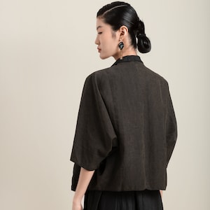 May include: A woman wearing a brown linen jacket with a black linen skirt. She is wearing black earrings with a gold accent.