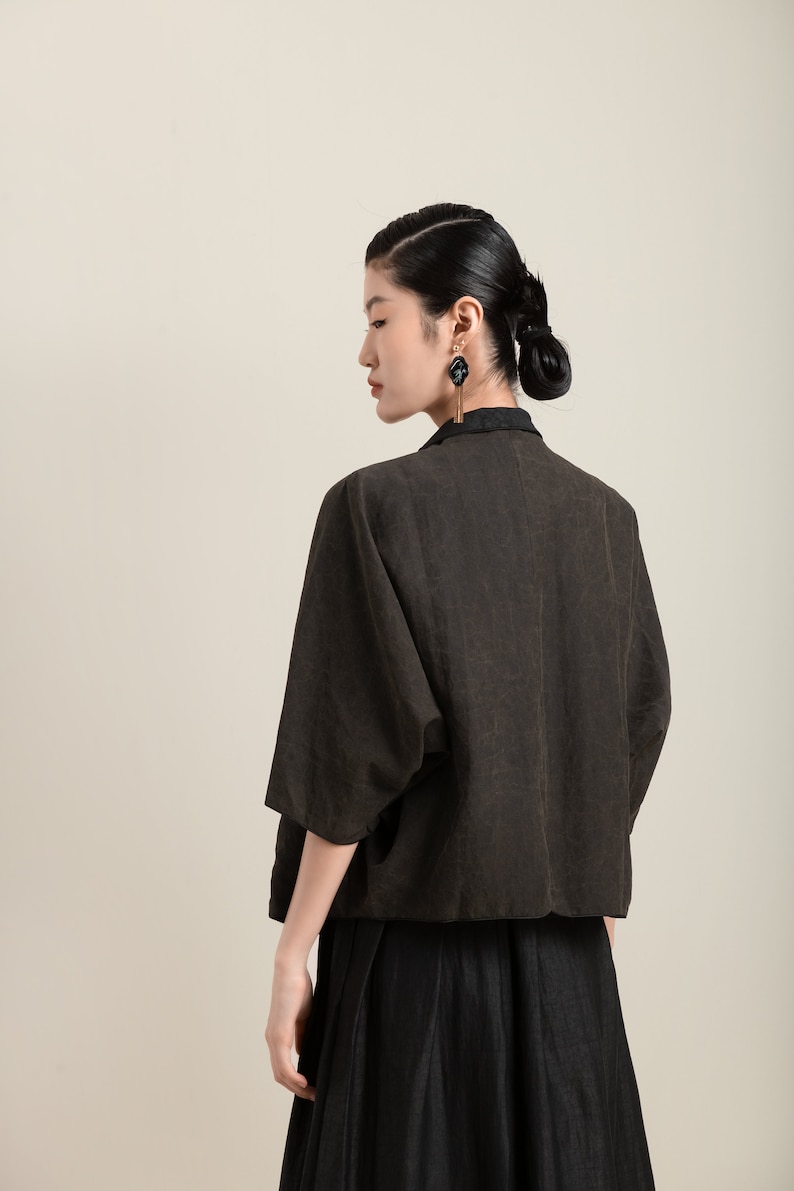 May include: A woman wearing a brown linen jacket with a black linen skirt. She is wearing black earrings with a gold accent.