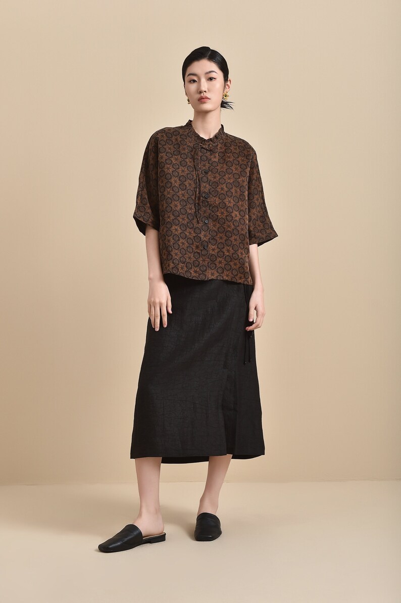 May include: A woman is wearing a brown and black patterned short-sleeved shirt with a black skirt and black slip-on shoes.
