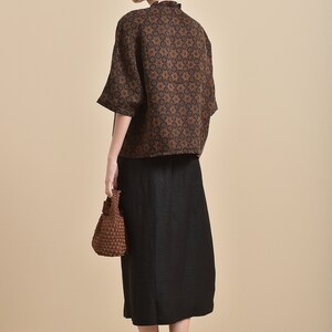 May include: A brown and black patterned short-sleeved blouse with a high neck and a black skirt. The woman is wearing a brown woven bag.