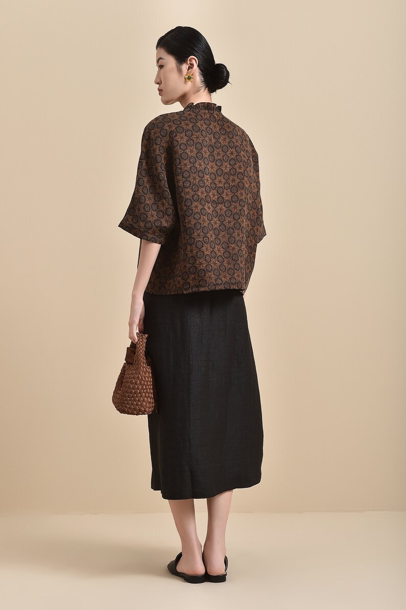 May include: A brown and black patterned short-sleeved blouse with a high neck and a black skirt. The woman is wearing a brown woven bag.