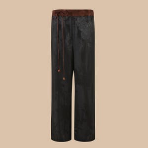 Op de afbeelding: Zwarte wijde broek met bloemenprint en een bruine tailleband.
