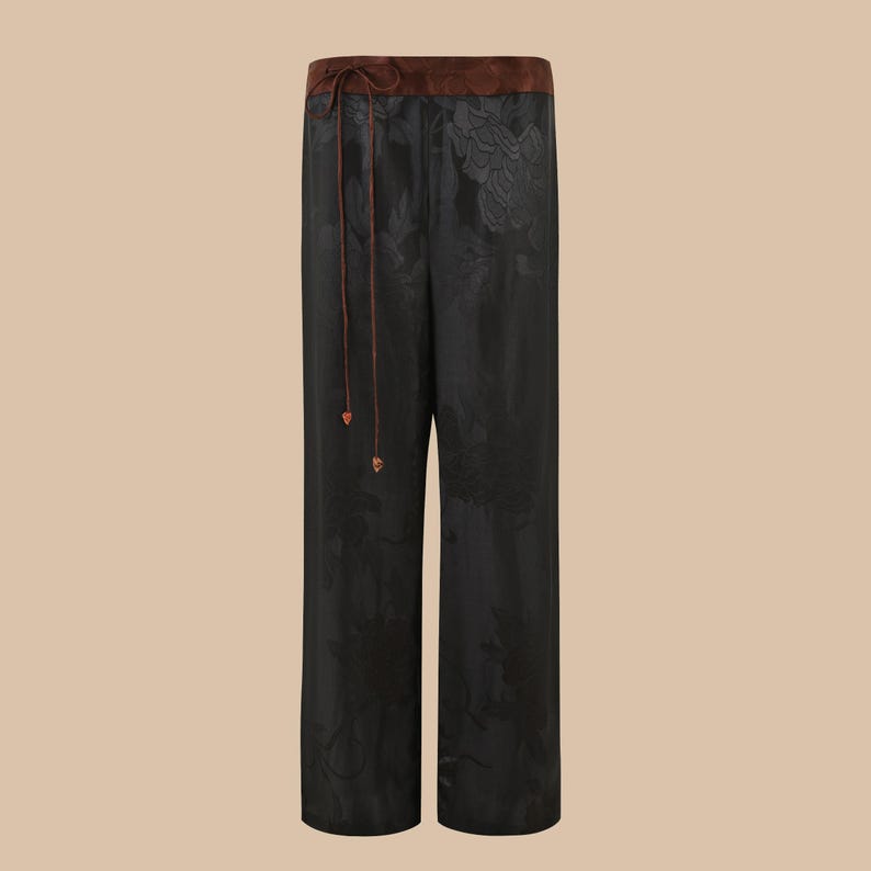 Op de afbeelding: Zwarte wijde broek met bloemenprint en een bruine tailleband.