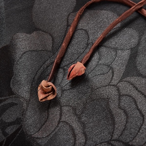 Op de afbeelding: Close-up van een donkere stof met een bloemenpatroon. Twee bruine leren koorden met rode uiteinden zijn aan elkaar gebonden.