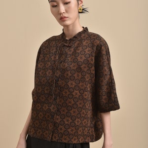 May include: A brown and black patterned blouse with a mandarin collar and a button closure. The blouse has a relaxed fit and three-quarter sleeves.