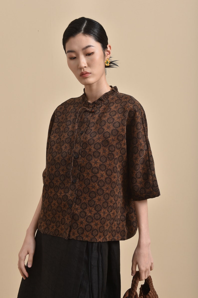 May include: A brown and black patterned blouse with a mandarin collar and a button closure. The blouse has a relaxed fit and three-quarter sleeves.