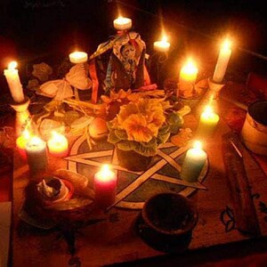 May include: A dimly lit scene featuring a table adorned with candles, flowers, and a pentagram. Various candles of different colors are lit, casting a warm glow. A small pot of flowers and other ritualistic items are present.