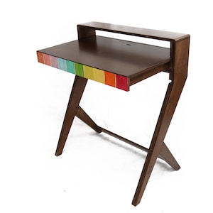 Puede incluir: Un escritorio de madera con acabado marrón oscuro y un acento de arcoíris en el borde frontal. El escritorio tiene un estante incorporado y patas anguladas. El escritorio mide aproximadamente 102 cm de ancho y 51 cm de profundidad.