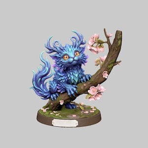 Puede incluir: Figura de fantasía de una criatura azul con ojos grandes, posada en una rama de árbol con flores rosas. La criatura tiene pelaje plumoso y una larga cola. La base es una plataforma circular con musgo.