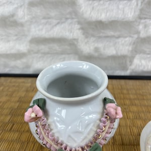 Puede incluir: Jarr&oacute;n de cer&aacute;mica blanca con cuerpo redondo y boca ancha. El jarr&oacute;n est&aacute; decorado con flores rosas, hojas verdes y ribetes dorados. El jarr&oacute;n tiene un patr&oacute;n texturizado en el cuerpo.