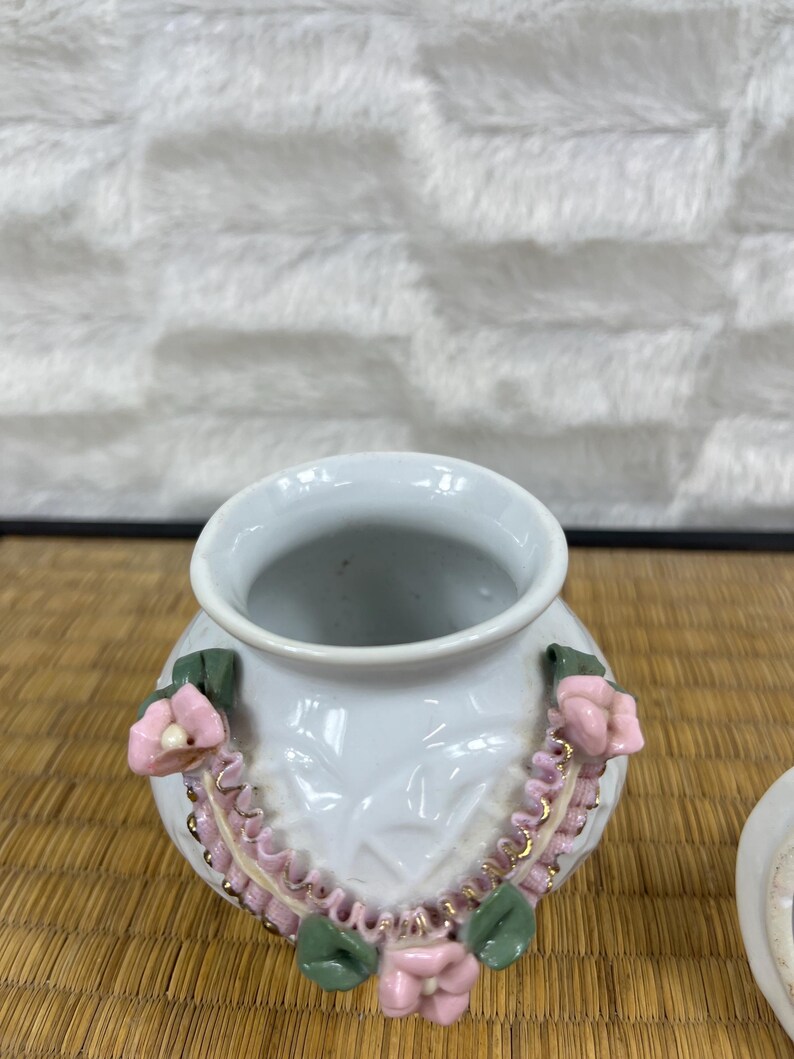 Puede incluir: Jarr&oacute;n de cer&aacute;mica blanca con cuerpo redondo y boca ancha. El jarr&oacute;n est&aacute; decorado con flores rosas, hojas verdes y ribetes dorados. El jarr&oacute;n tiene un patr&oacute;n texturizado en el cuerpo.