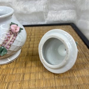 Puede incluir: Tarro de cer&aacute;mica blanca con tapa, decorado con detalles florales rosas y ribete dorado. El tarro tiene un patr&oacute;n texturizado, similar a un tejido de mimbre. La tapa est&aacute; quitada.