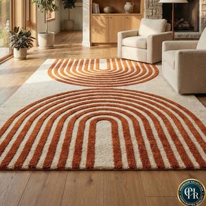 May include: A rectangular area rug featuring a cream-colored base with two large, symmetrical, rust-orange arched patterns. The design consists of concentric semi-circular lines that create a bold, repeating geometric motif across the surface.