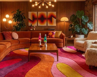 May include: A living room featuring a large curved orange sofa, a wooden coffee table with two lava lamps, and a plush area rug with wavy patterns in shades of pink, orange, red, and yellow. A sputnik chandelier hangs above, with two large potted plants.