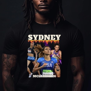 May include: A black t-shirt featuring a graphic of Sydney McLaughlin, an American track and field athlete, running in a race. The graphic includes the text "Sydney McLaughlin" and "USA".