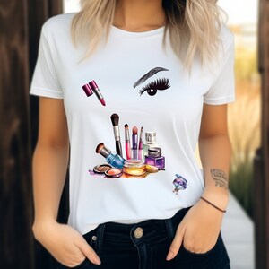 Op de afbeelding: Wit T-shirt met een kleurrijke afbeelding van make-upkwasten, lippenstift, oogschaduw en een gestileerd oog met wimpers.