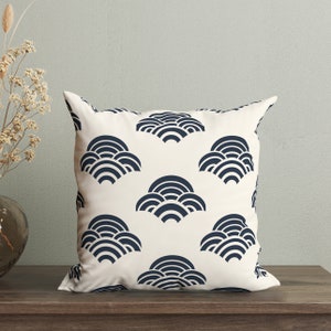 May include: A white throw pillow with a navy blue geometric pattern of overlapping semi-circles. The pillow is on a wooden surface.