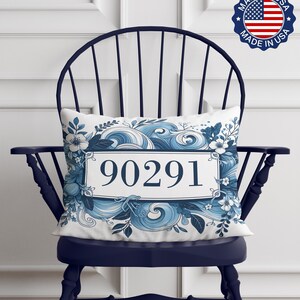 May include: A white pillow with a blue and white floral design and the number 90291 in a white rectangle. The pillow is sitting on a navy blue chair.