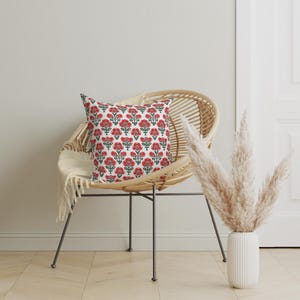 Puede incluir: Una silla de mimbre blanca con un coj&iacute;n estampado floral rojo y verde. La silla est&aacute; sobre un suelo de madera clara. Un jarr&oacute;n con hierba de la pampa seca est&aacute; en el fondo.