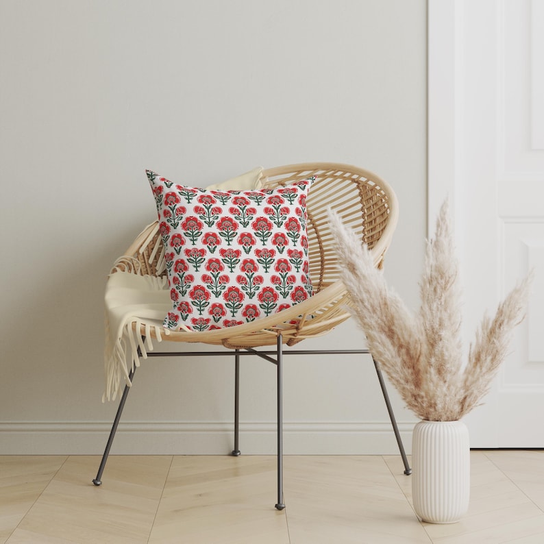 Puede incluir: Una silla de mimbre blanca con un coj&iacute;n estampado floral rojo y verde. La silla est&aacute; sobre un suelo de madera clara. Un jarr&oacute;n con hierba de la pampa seca est&aacute; en el fondo.