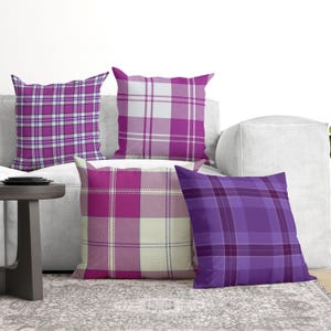 May include: Four square throw pillows featuring various plaid patterns in shades of purple, magenta, and white. The designs include intersecting lines and checkered blocks, creating a coordinated set of decorative cushions with distinct geometric motifs.