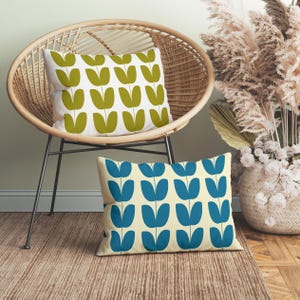 Op de afbeelding: Twee decoratieve kussens met een geometrisch patroon van gestileerde bloemen. Het kussen aan de linkerkant heeft een witte achtergrond met groene bloemen. Het kussen aan de rechterkant heeft een crèmekleurige achtergrond met blauwe bloemen.