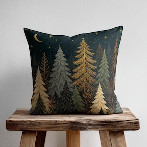 May include: A square throw pillow featuring a dark navy blue night sky background with a golden crescent moon and stars. The design displays a dense forest of evergreen trees in shades of gold, sage green, and dark brown with fine line details.