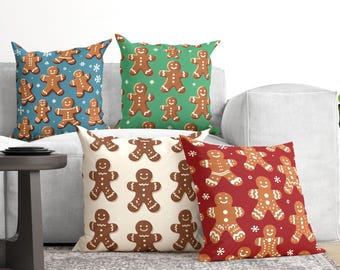 May include: Four square throw pillows featuring repeating gingerbread man patterns. One pillow is blue, one is green, one is cream, and one is red. Each pillow displays white snowflake accents scattered among the brown gingerbread figures.