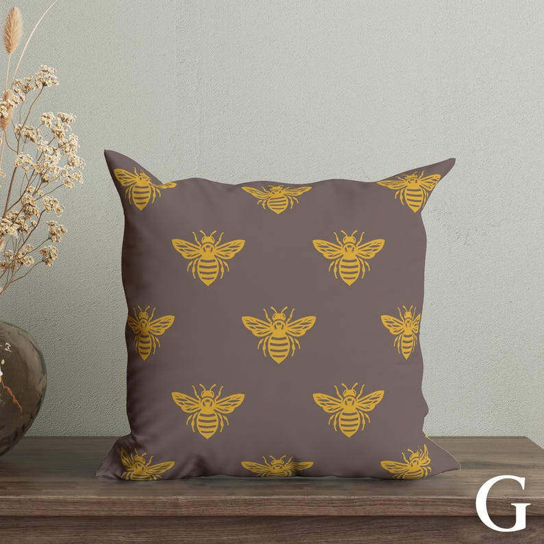 Puede incluir: Un coj&iacute;n decorativo cuadrado con un patr&oacute;n repetido de abejas amarillas sobre un fondo marr&oacute;n. El coj&iacute;n est&aacute; hecho de tela suave y est&aacute; dise&ntilde;ado para la decoraci&oacute;n del hogar.