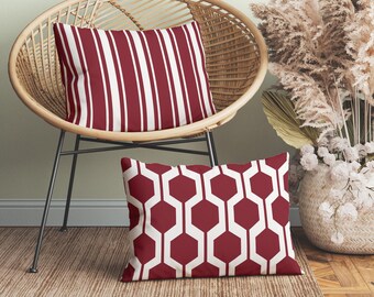May include: Two rectangular throw pillows featuring a deep red and white color scheme. One pillow displays a vertical striped pattern, while the other pillow showcases a repeating geometric hexagonal lattice design in the same red and white colors.