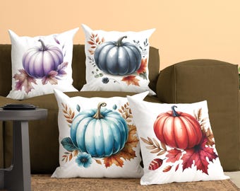 May include: Four square throw pillows with white backgrounds, each featuring a single pumpkin illustration in purple, dark blue, light blue, or red, accented with colorful autumn leaves and botanical elements in a watercolor art style.