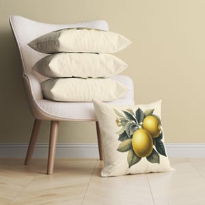 Puede incluir: Un conjunto de cuatro almohadas blancas con una sola almohada que presenta una ilustración vintage de limones en una rama. Las almohadas están dispuestas en un sillón blanco con patas de madera.