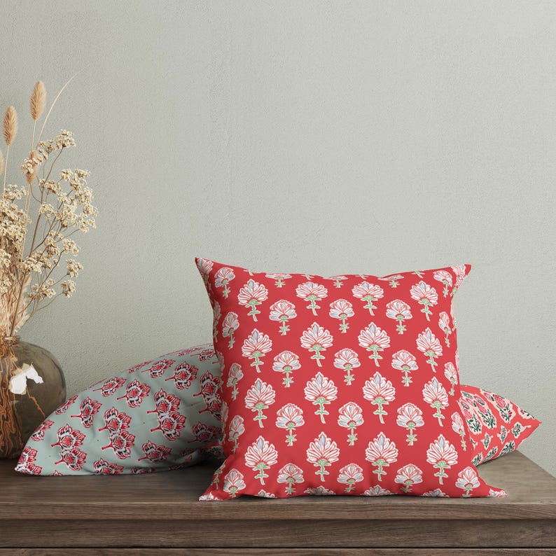 Puede incluir: Dos almohadas decorativas con patrones florales. La almohada delantera es roja con flores blancas y la almohada trasera es verde con flores blancas.