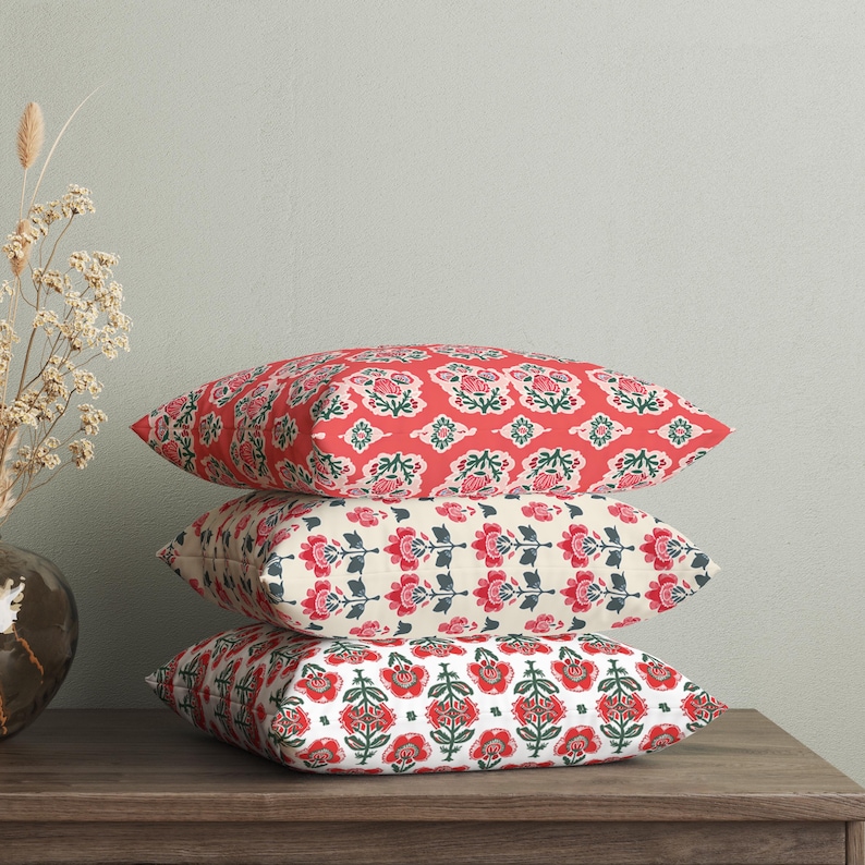Puede incluir: Tres almohadas decorativas con patrones florales. La almohada superior es roja con un dise&ntilde;o floral blanco y verde. La almohada del medio es crema con un dise&ntilde;o floral rojo y verde. La almohada inferior es blanca con un dise&ntilde;o floral rojo y verde.
