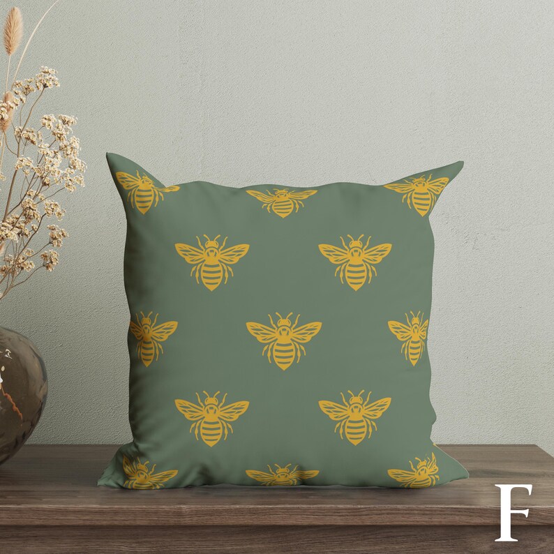 Puede incluir: Un coj&iacute;n decorativo cuadrado con un patr&oacute;n repetido de abejas amarillas sobre un fondo verde apagado. El coj&iacute;n est&aacute; hecho de tela suave y est&aacute; dise&ntilde;ado para la decoraci&oacute;n del hogar.