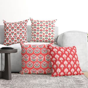 May include: Four square throw pillows arranged on a sofa. Two pillows feature a white background with a repeating red and green floral pattern. The other two pillows have a solid red background with repeating white and green floral motifs.