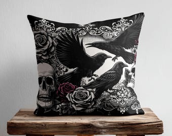 May include: A square throw pillow featuring a detailed black and white graphic print of two ravens, one in flight and one perched, surrounded by intricate floral patterns, blooming roses, and two human skulls on a dark background.