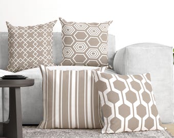 May include: A set of four square throw pillows featuring beige and white geometric patterns. One pillow has a diamond grid, one has a nested hexagon design, one has vertical stripes, and one has a large-scale interlocking hexagon pattern.