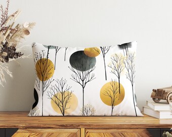 Puede incluir: Un cojín rectangular con fondo blanco que presenta un patrón repetitivo de árboles dibujados con líneas negras y formas circulares sólidas en tonos amarillo mostaza, gris oscuro y oro claro, creando un diseño visual equilibrado y gráfico.