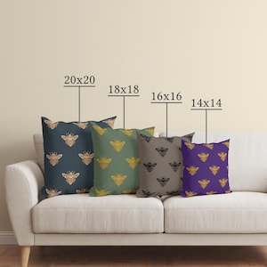 Puede incluir: Cuatro cojines decorativos con dise&ntilde;os de abejas en azul marino, verde, gris y morado. Tama&ntilde;os: 50x50, 45x45, 40x40 y 35x35 cm. Los cojines est&aacute;n colocados en un sof&aacute; blanco.