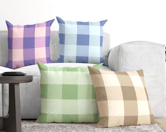 May include: Four square throw pillows featuring a classic buffalo check pattern. The pillows are colored in light purple and pink, light blue and white, light green and white, and tan and white, arranged in a group on a light gray sofa.