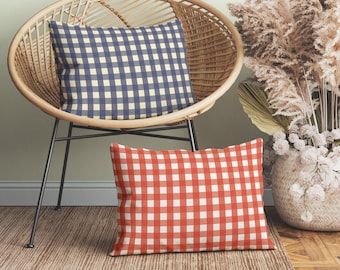 May include: Two rectangular throw pillows featuring a classic gingham check pattern. One pillow is navy blue and cream, while the other is red and white. Both pillows have a simple, clean design with a consistent grid of squares across the fabric surface.
