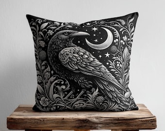 May include: A square throw pillow featuring a black and white illustration of a raven perched among intricate botanical patterns, leaves, and berries. Above the bird, a crescent moon and several small stars are depicted against a dark background.