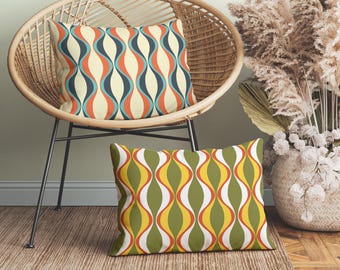 Op de afbeelding: Twee decoratieve kussens met een retro, golvend patroon. Het kussen aan de linkerkant heeft een blauw, oranje en wit patroon. Het kussen aan de rechterkant heeft een groen, oranje en wit patroon.