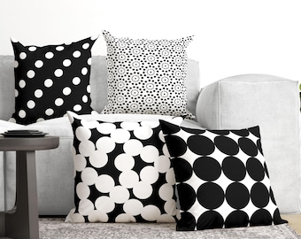 May include: Four square throw pillows featuring black and white geometric patterns. One pillow has large white polka dots on black, another has small dot clusters, one has overlapping white circles, and the last has a grid of large black circles.