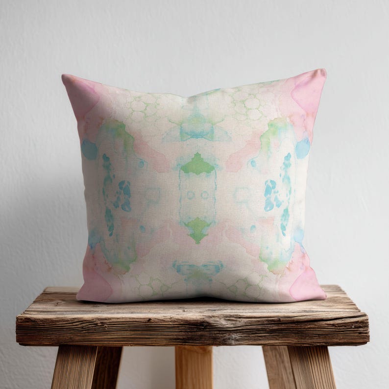 A decorative throw pillow with a colorful abstract pattern sits on a wooden stool against a white wall.